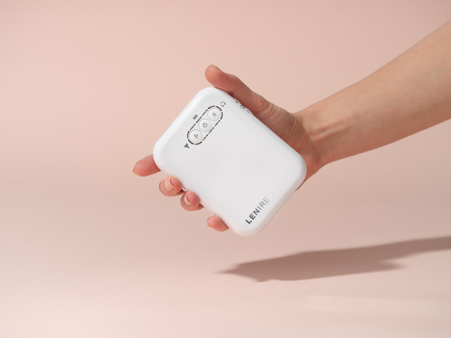 Lenire device held by hand and arm in frame, isolated on a pink background
