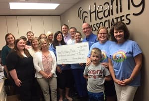 Large group of people at Hearing Associates office holding a ceremonial check