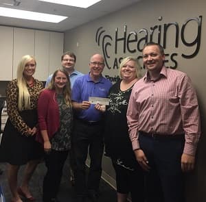 Group of people posing for photo in Hearing Associates office while holding a ceremonial check