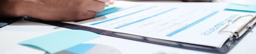 Person writing on a clipboard containing insurance forms