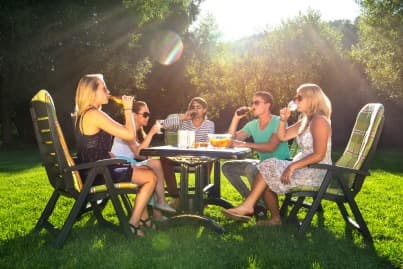 Five friends sitting around outdoor table enjoying cold drinks on a sunny day