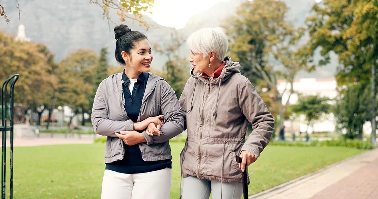 daughter holding arms with her elderly mother while going for a walk