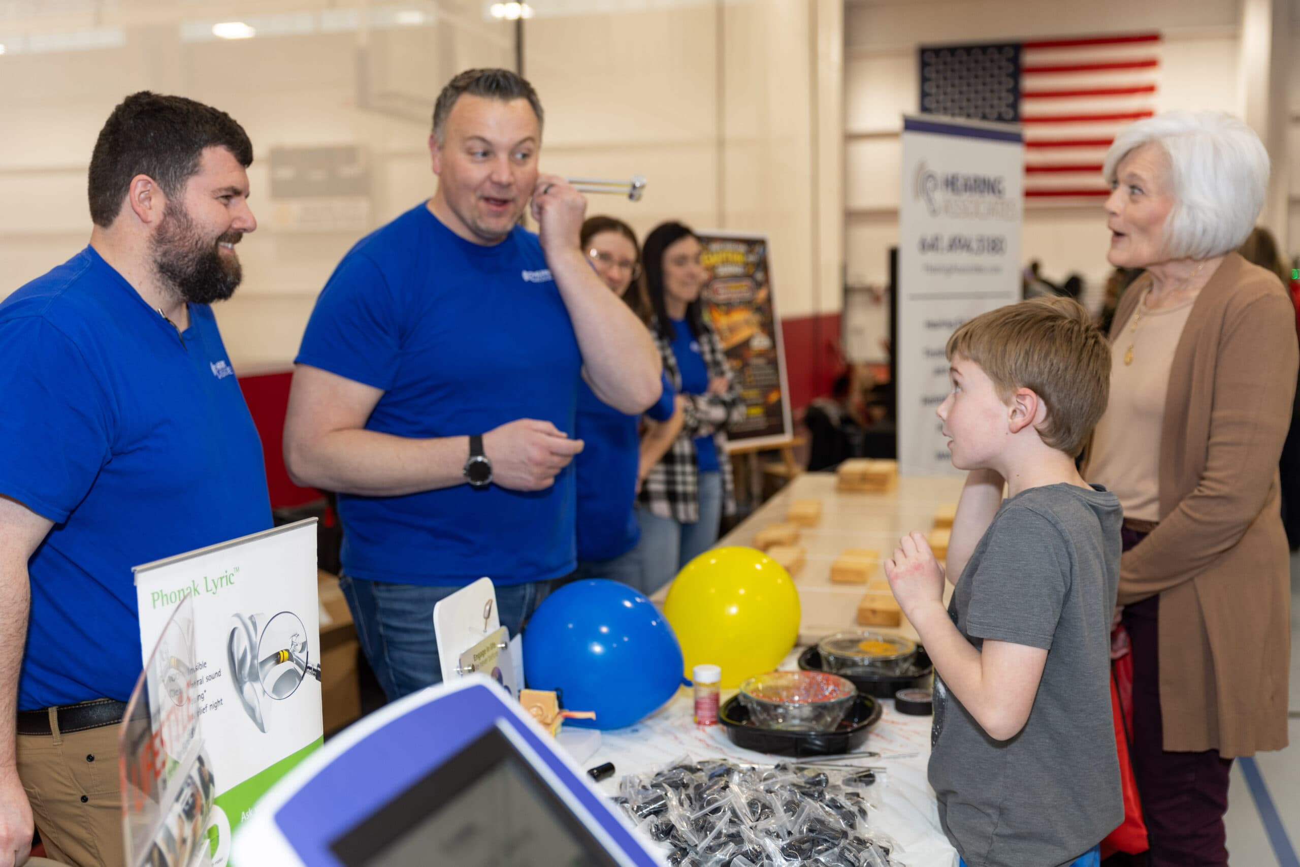 Hearing Associates Audiologist Bryce Phillip and President Alex Crippin talking about hearing with a young boy and a woman at their booth at the North Iowa STEM Festival.