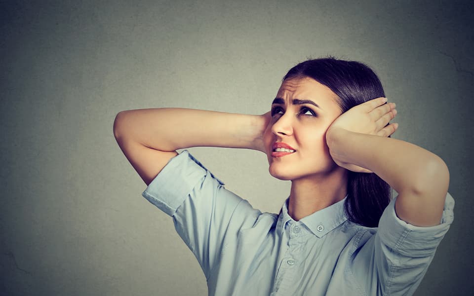 woman covering both of her ears with her hands showing discomfort