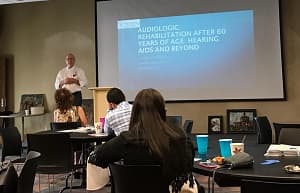 Speaker presenting to an audience while standing next to a projection screen