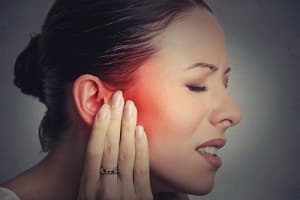 Woman in pain with hand on head experiencing tinnitus symptoms