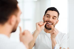 Image of a man looking at his reflection in a mirror while he flosses.