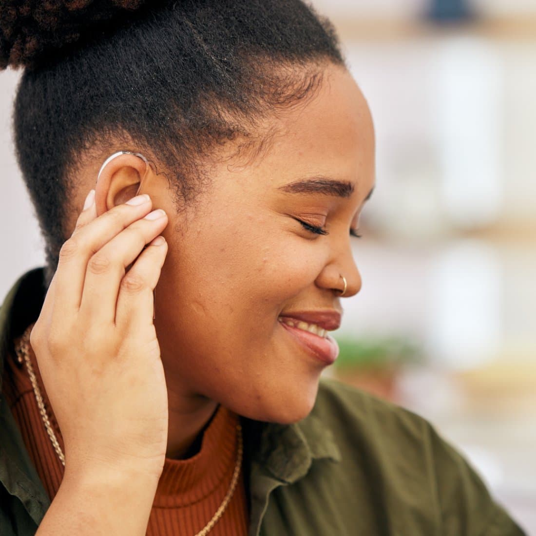 Woman smiling while adjusting her behind-the-ear hearing aid