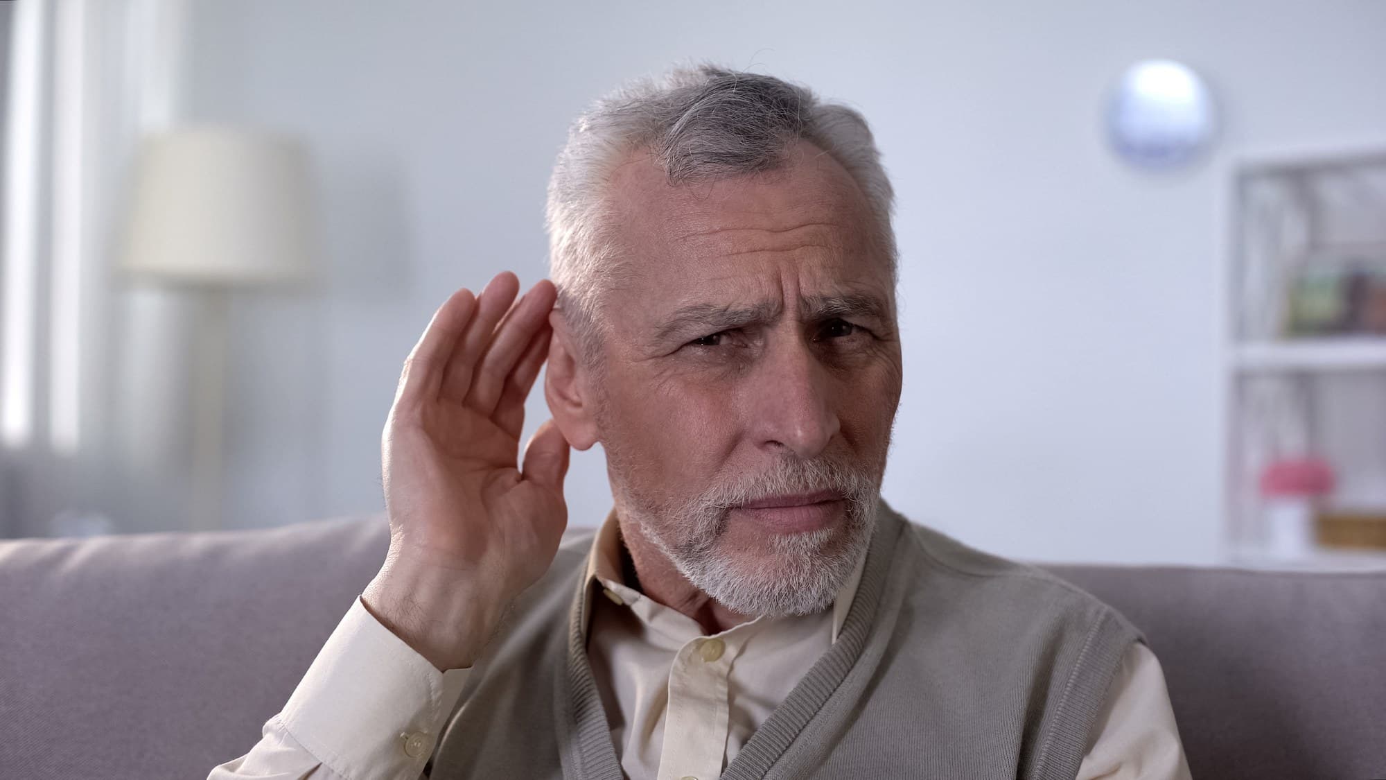 Senior man cupping his hand behind his ear, straining to hear a conversation