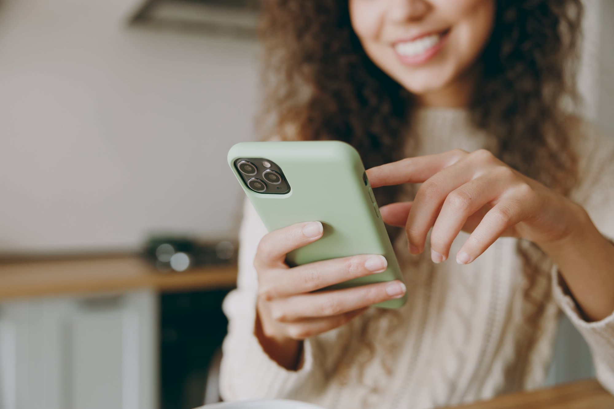 Smiling woman with curly hair holding a smartphone to pair it with her Bluetooth hearing aids
