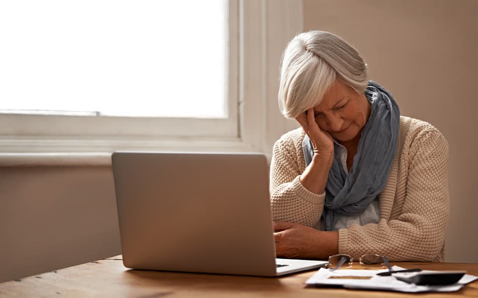 A stressed senior woman sitting at a table and looking at her laptop