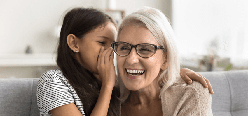 little girl whispering in her grandmas ear causing laughter